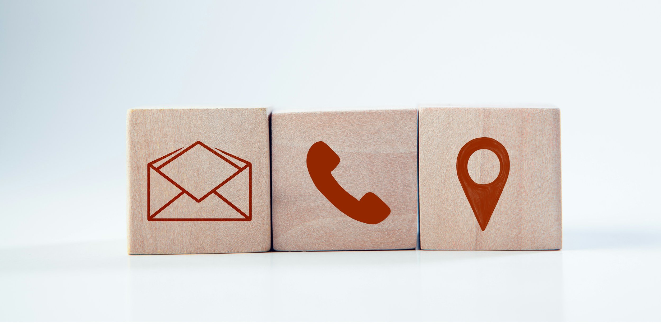 Three wooden blocks with contact icons: email on the left, phone in the middle, and location pin on the right.