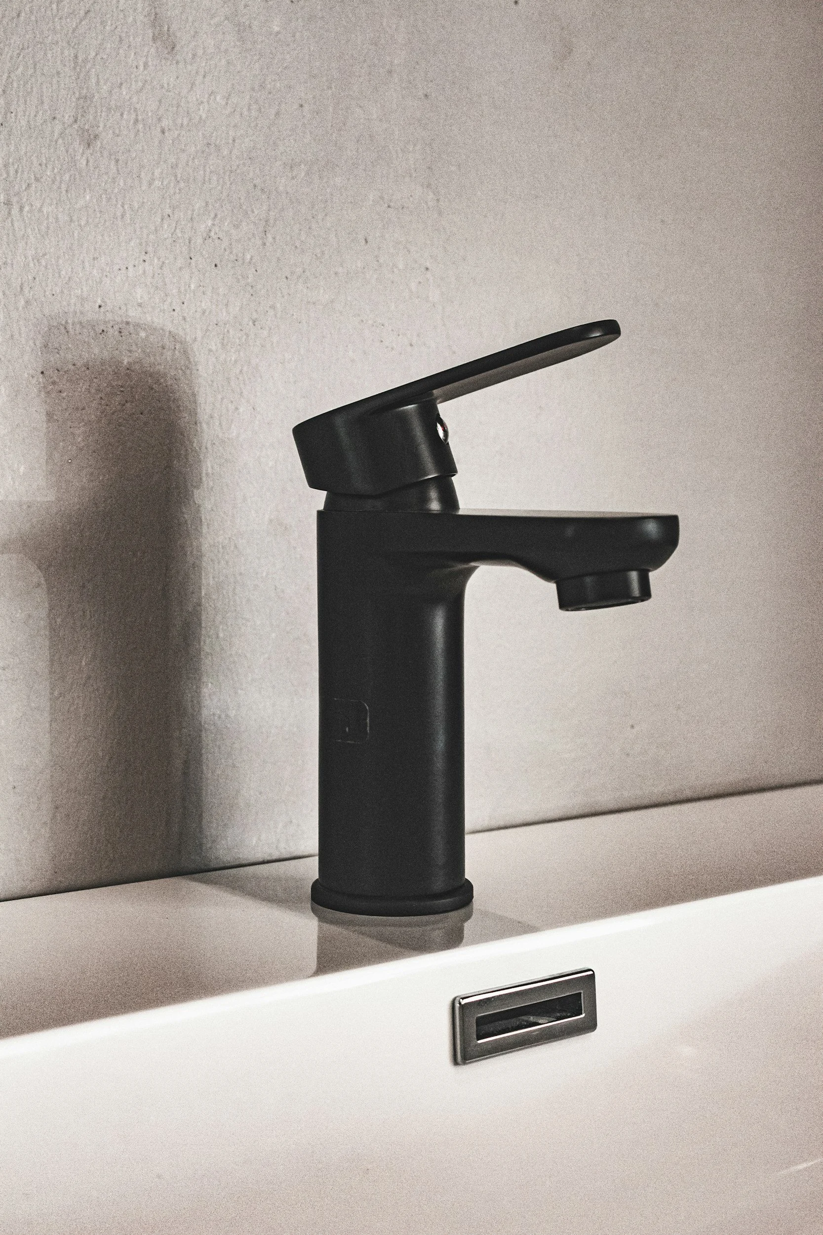 Close-up of a black modern faucet installed on a white countertop against a textured wall.