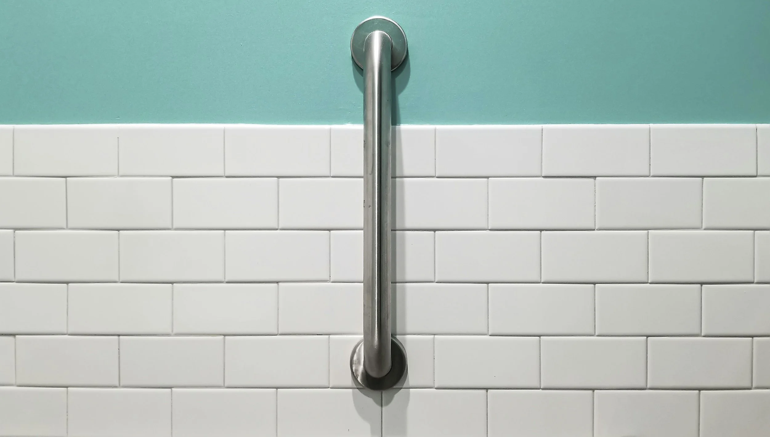 Metal handrail mounted on a wall with teal paint above and white subway tiles below.