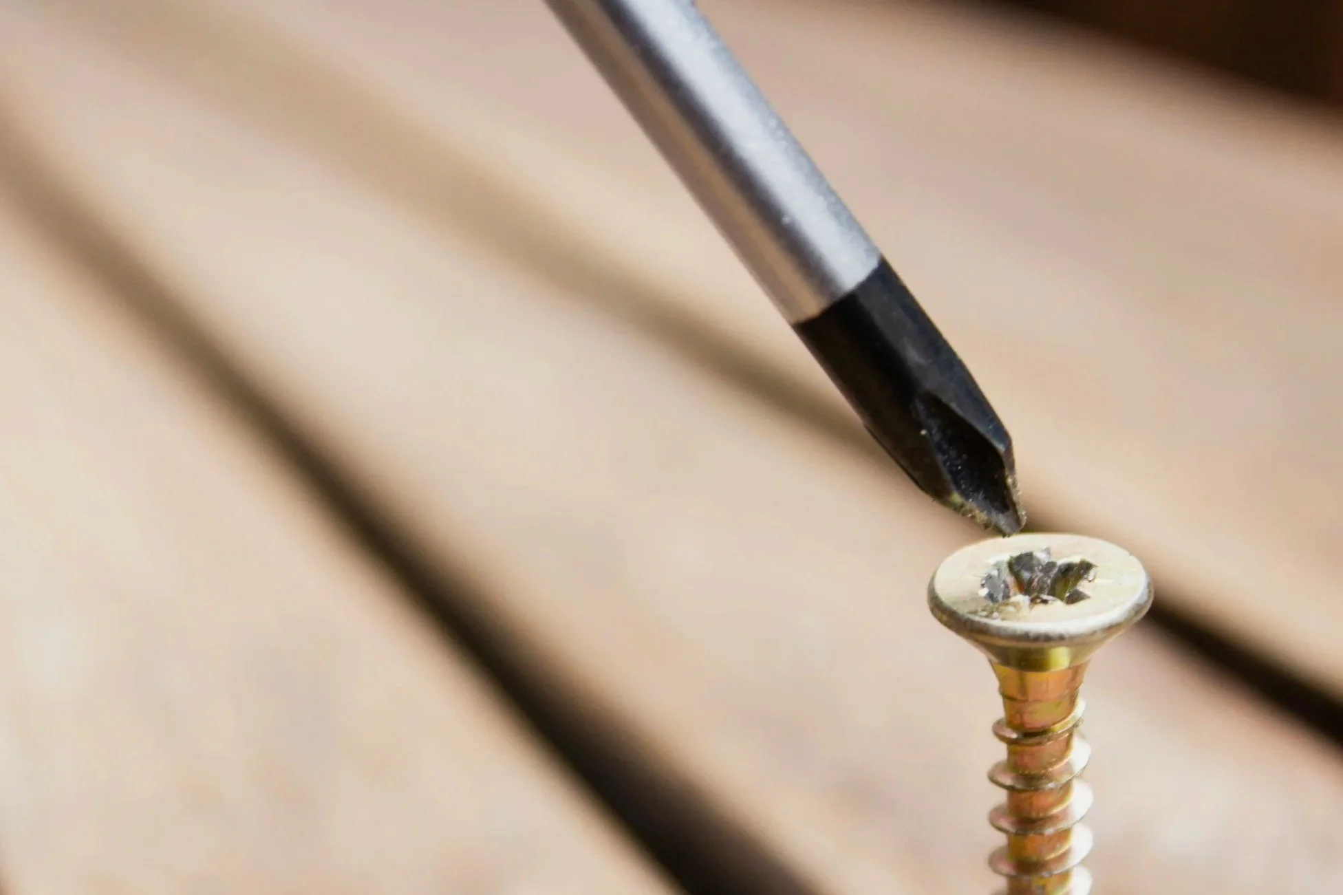 Close-up of a metal screw securing a small decorative item, possibly a button or ornament, onto a wooden surface.