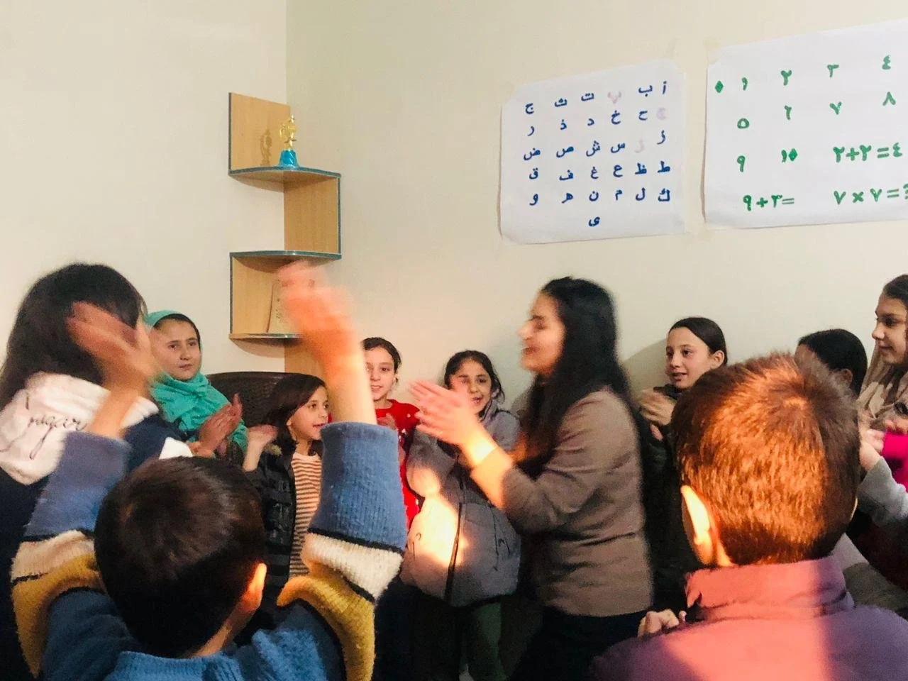 Group of children and a woman in a classroom, engaged in a group activity or celebration.