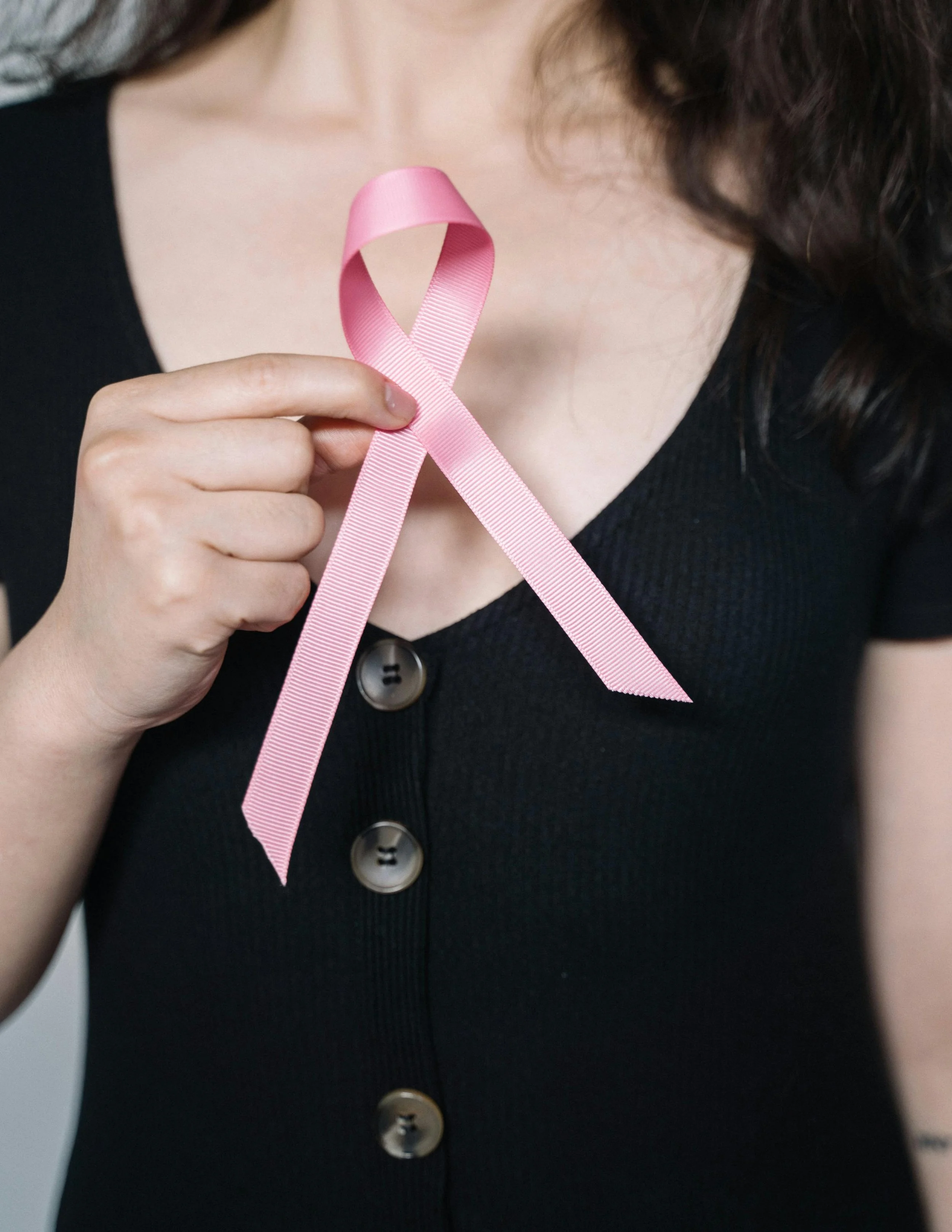 A woman holding a pink ribbon in front of her chest, which is associated with breast cancer awareness.