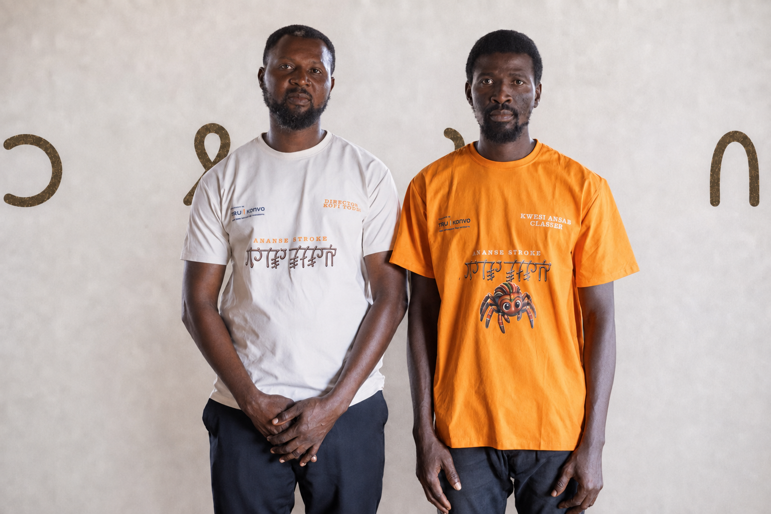 Two men standing indoors against a beige wall, one in a white T-shirt and the other in an orange T-shirt, both with serious expressions and looking at the camera.