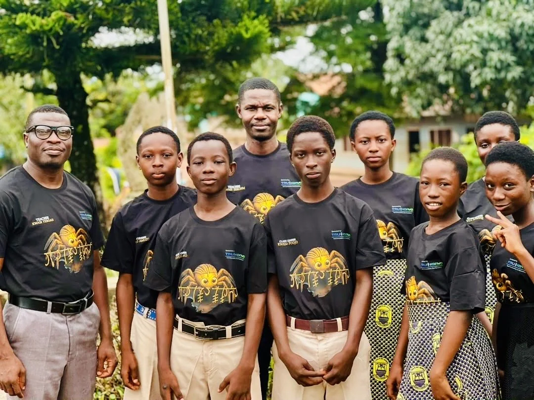 A group of nine young students and two adults posing outdoors, wearing matching black t-shirts with a lion graphic and text.