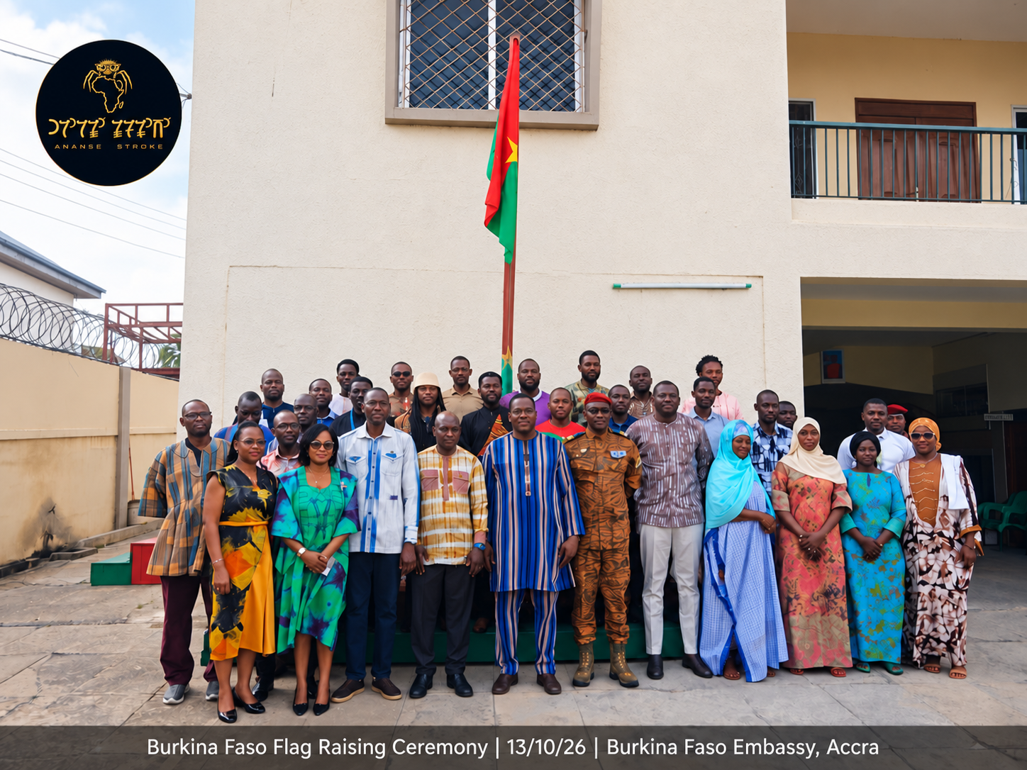 A group of people standing in front of the Burkina Faso embassy building, participating in a flag raising ceremony, with a Burkina Faso flag prominently displayed above them.