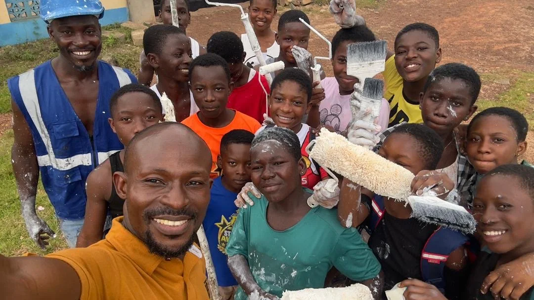 Ananse Stroke Foundation Teachers and students, smiling, holding paintbrushes with paint, outdoors after painting Ananse a new home.