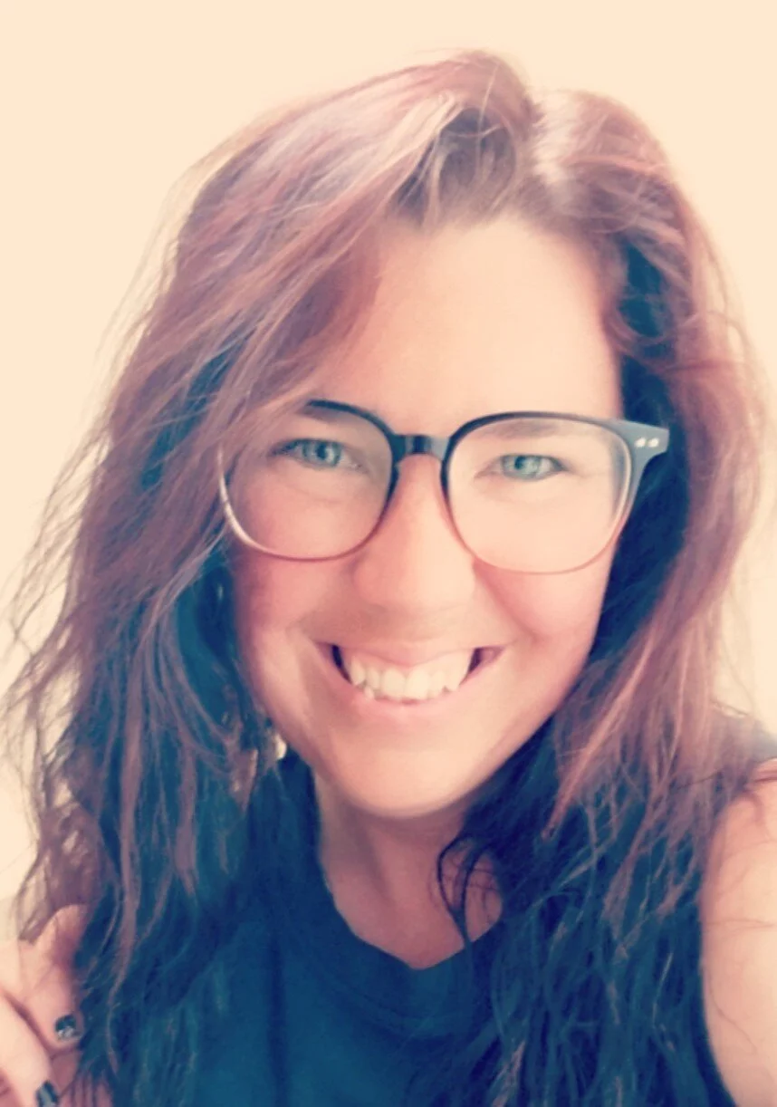A woman with long, wavy red hair and glasses smiling at the camera.