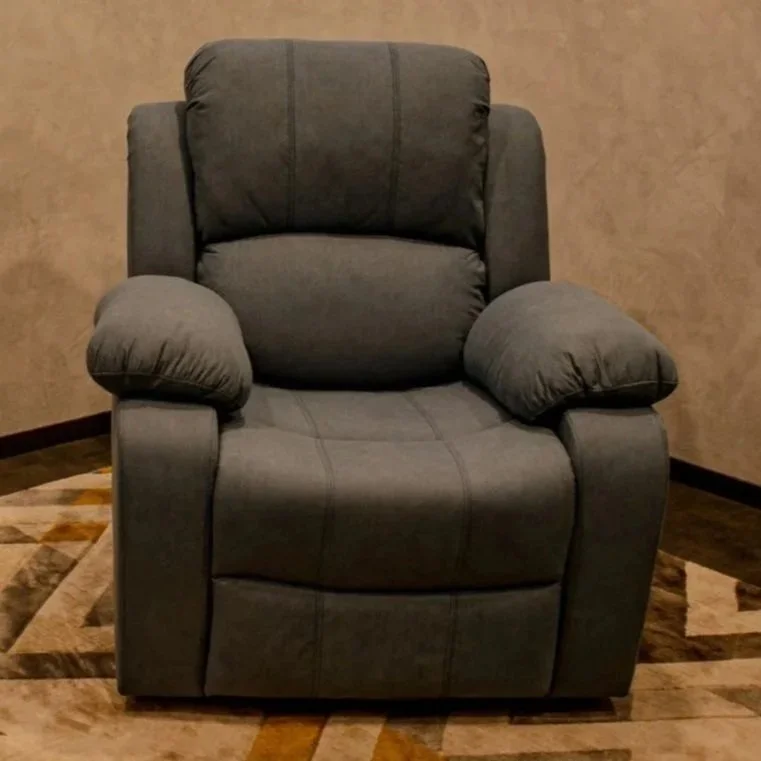 A gray upholstered armchair with padded armrests placed on a multicolored geometric patterned rug, against a beige wall.