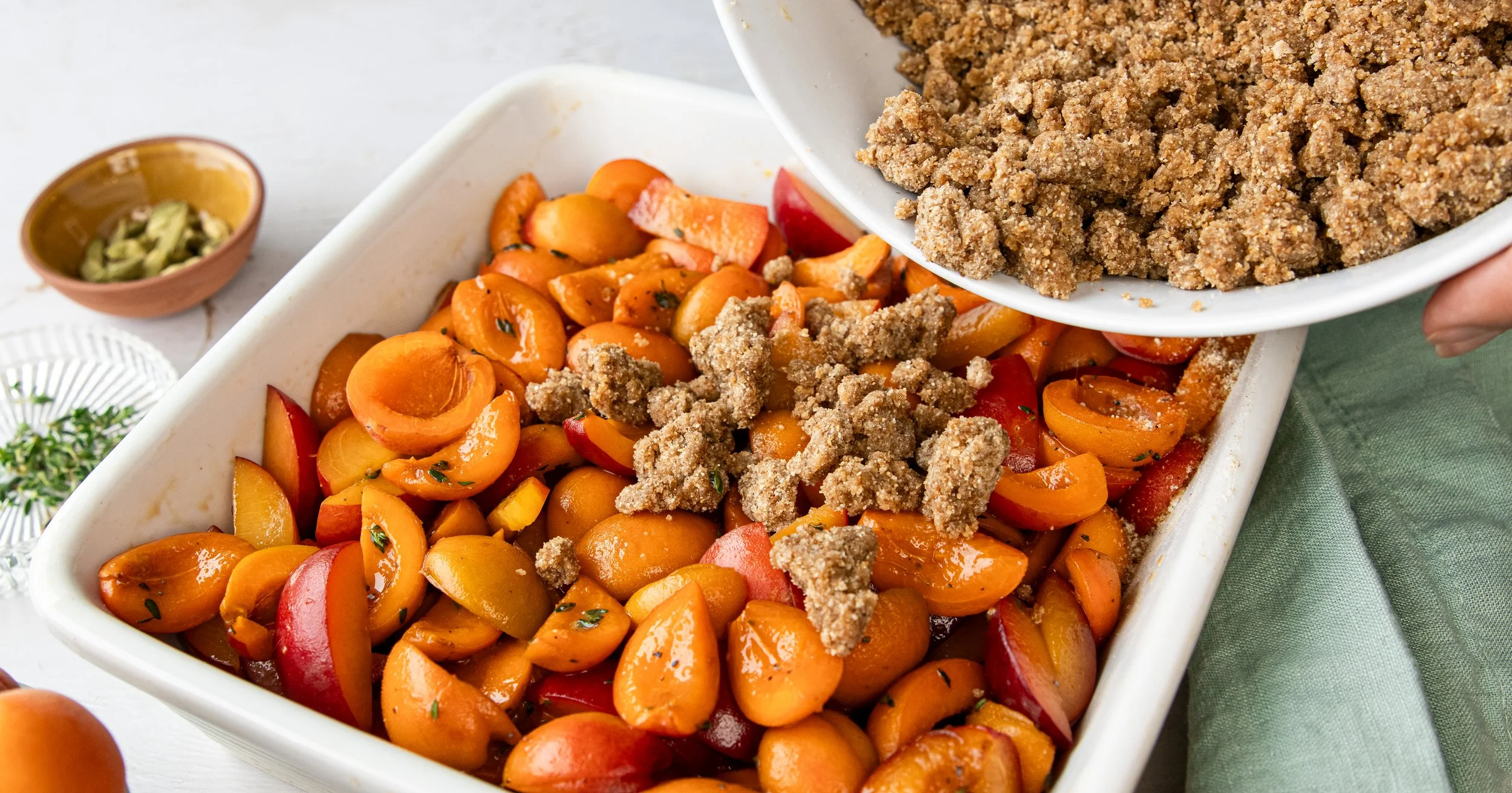 Peach and nectarine fruit crumble with ground nut topping in a white baking dish, with a small bowl of chopped nuts in the background.