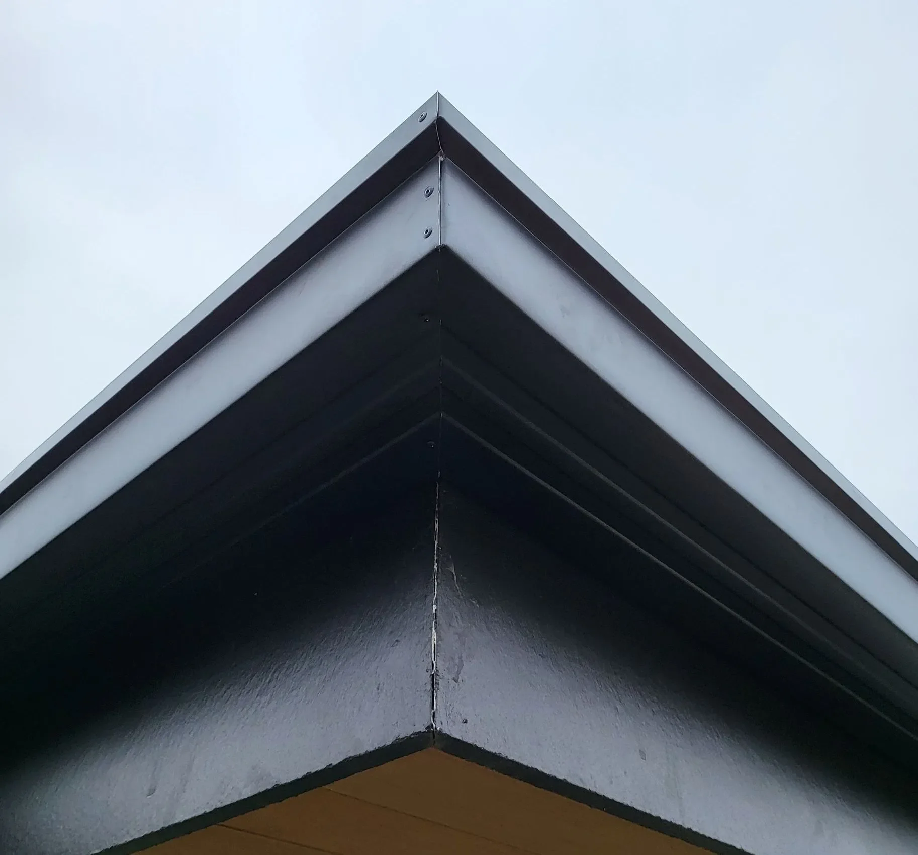 Close-up of the corner of a modern building's roof with black and white exterior panels, pointed upward against a cloudy sky.