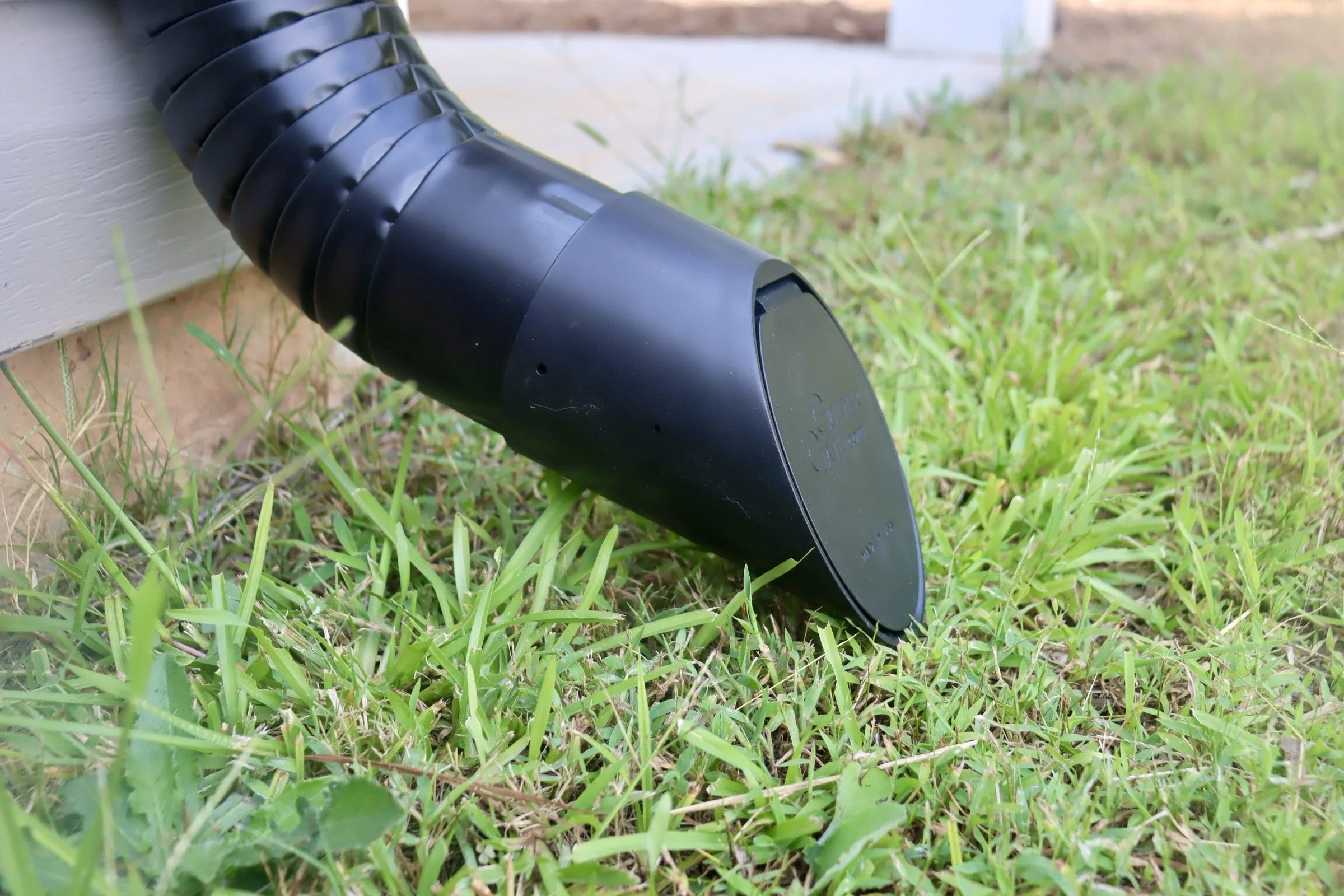 A black microphone pointing towards the grass outdoors near the corner of a white structure.