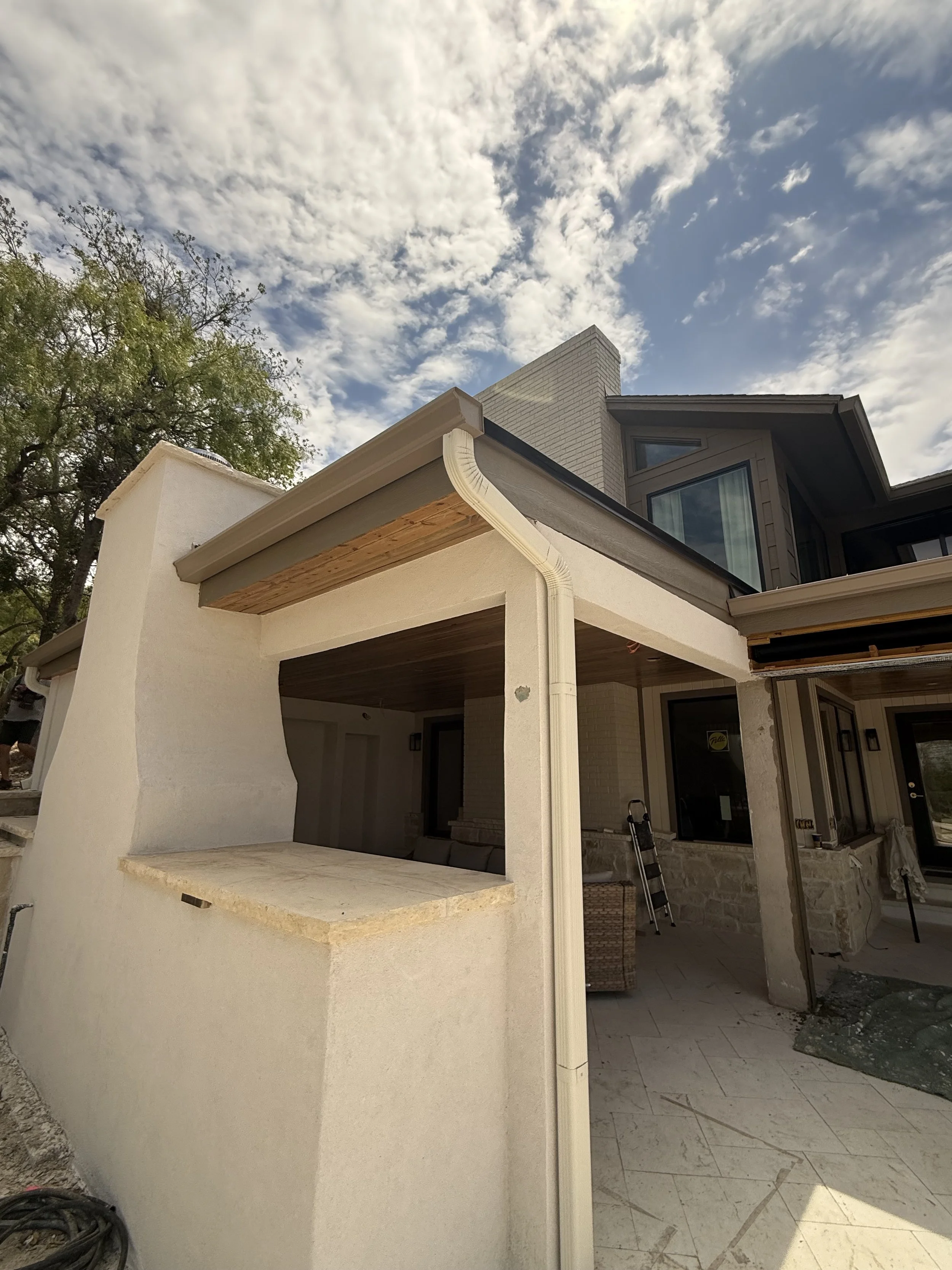 Partially constructed house with a white exterior wall, a wooden and concrete counter, and large windows, under a cloudy sky.