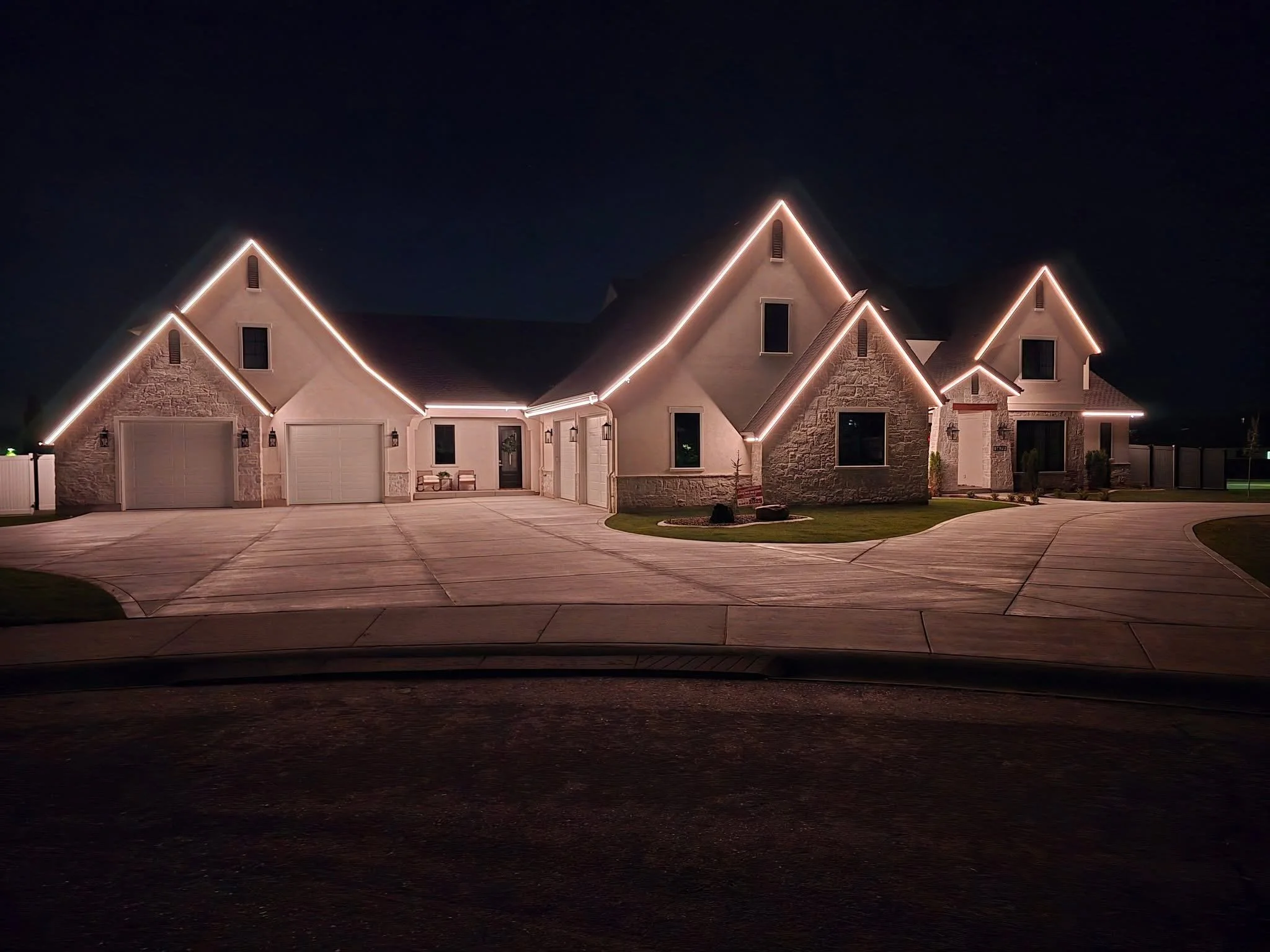 Night view of a house with illuminated roofline, a garage door, and a front yard, under a dark sky.