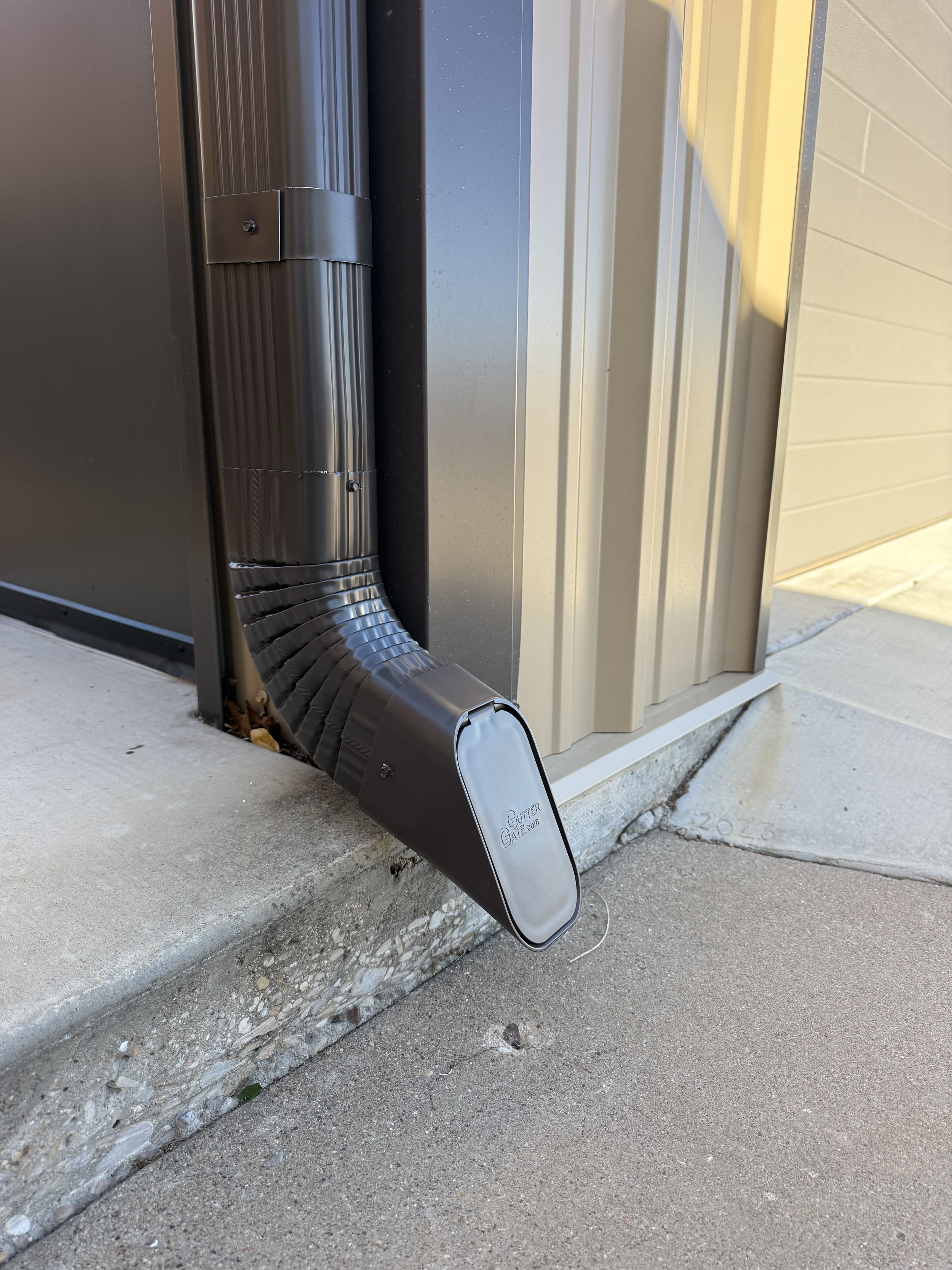 Close-up of a gutter protection system installed on a house, showing a black lid with the brand name 'GutterGator' on it, attached to a metal gutter and downspout.