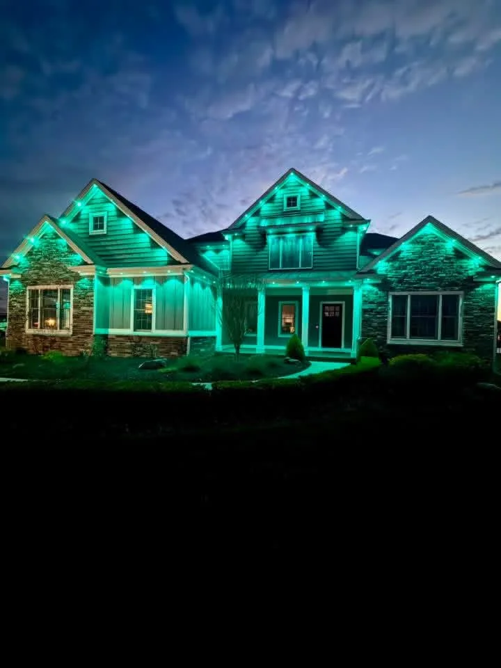 A house decorated with green Christmas lights, with a dark blue evening sky in the background.