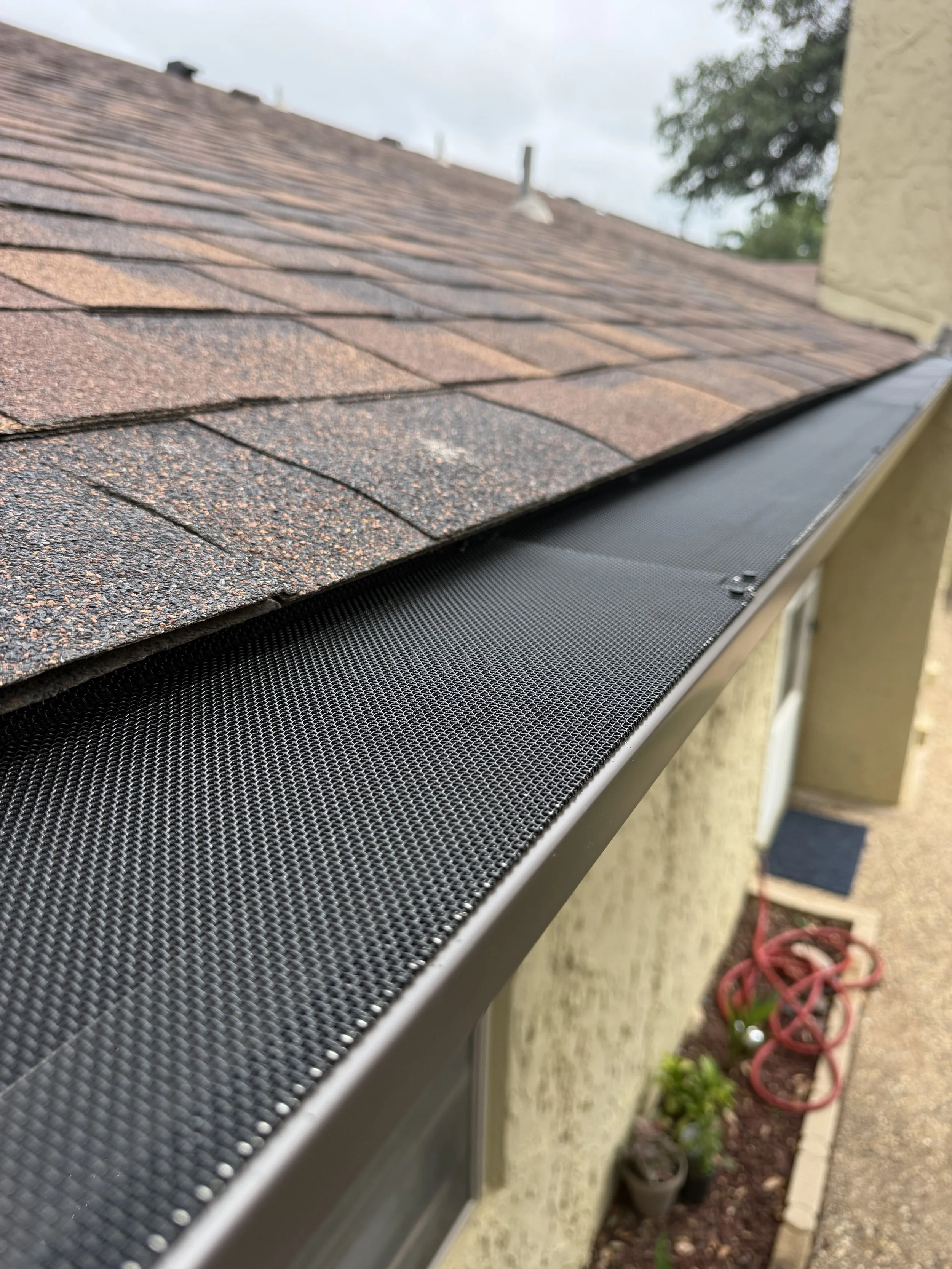 Close-up of a house roof with asphalt shingles and a gutter, seen from the side during daytime.