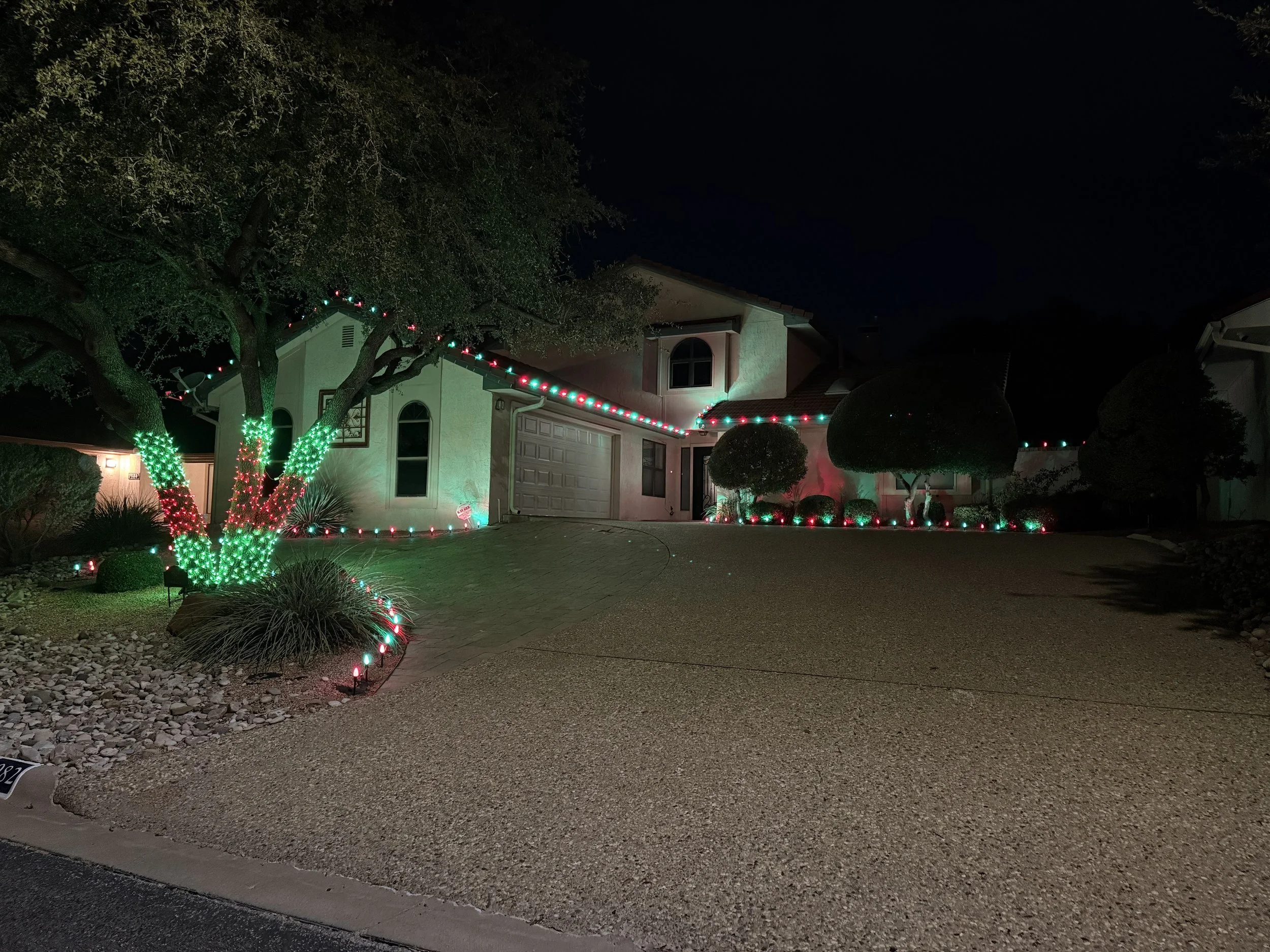 A house decorated with multicolored Christmas lights, with illuminated trees and a dark night sky.