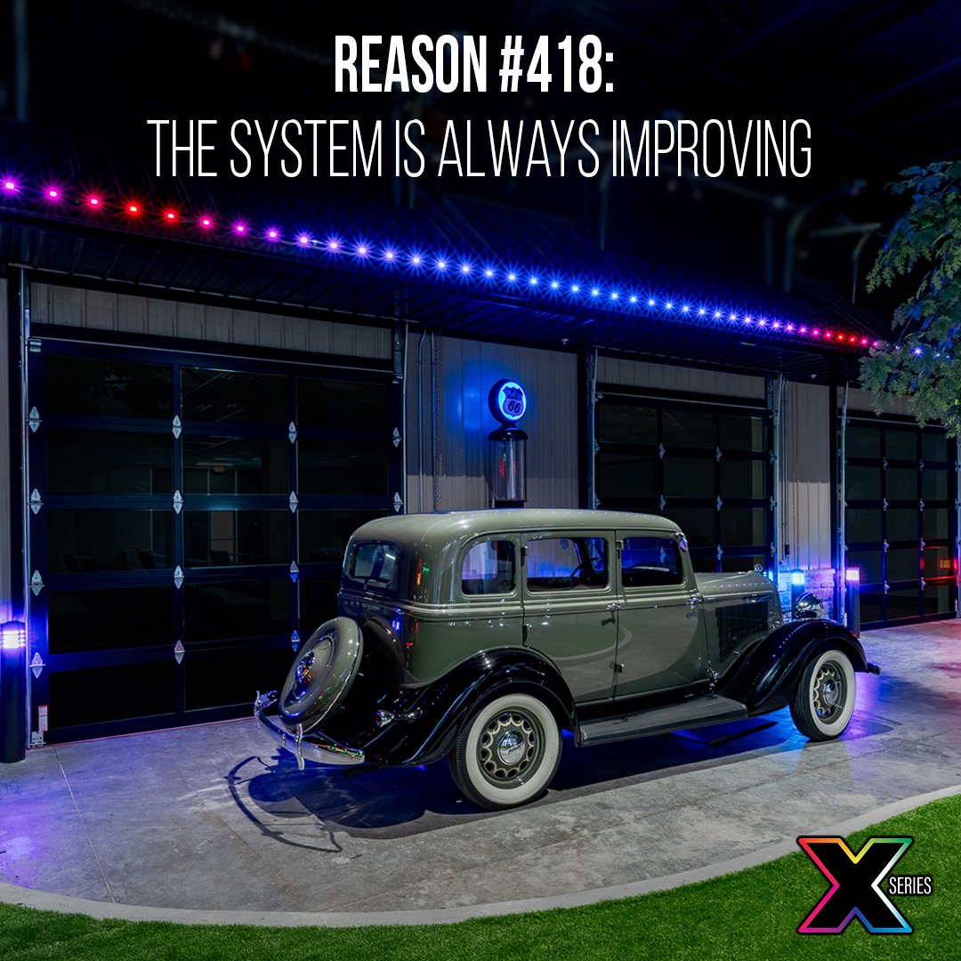 Vintage car parked outside a modern building with colorful LED lights and a Route 66 sign at night.