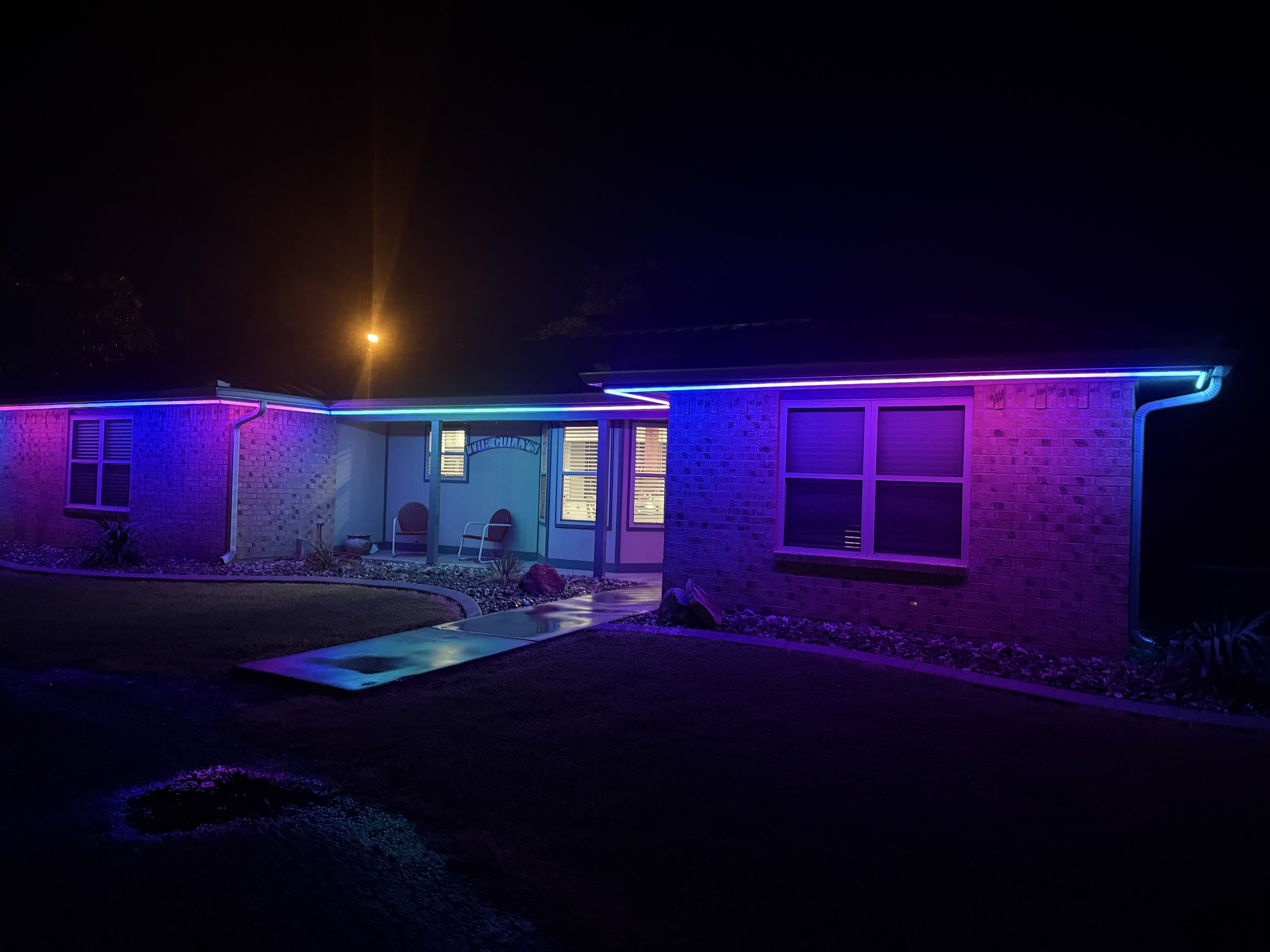 A house decorated with vibrant blue, pink, and purple neon lights outlining the roof and windows at night.
