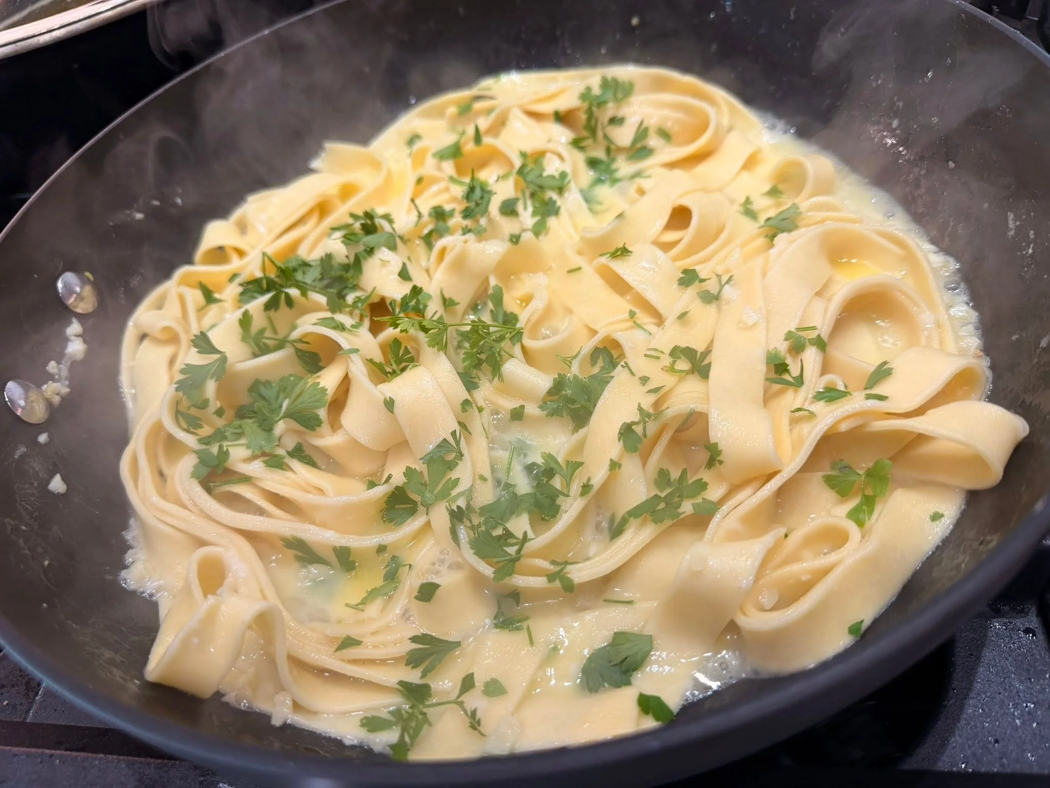 A bowl of cooked fettuccine pasta topped with chopped parsley in a creamy sauce.