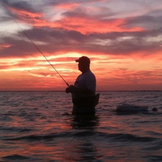 A person fishing in the water during a colorful sunset.
