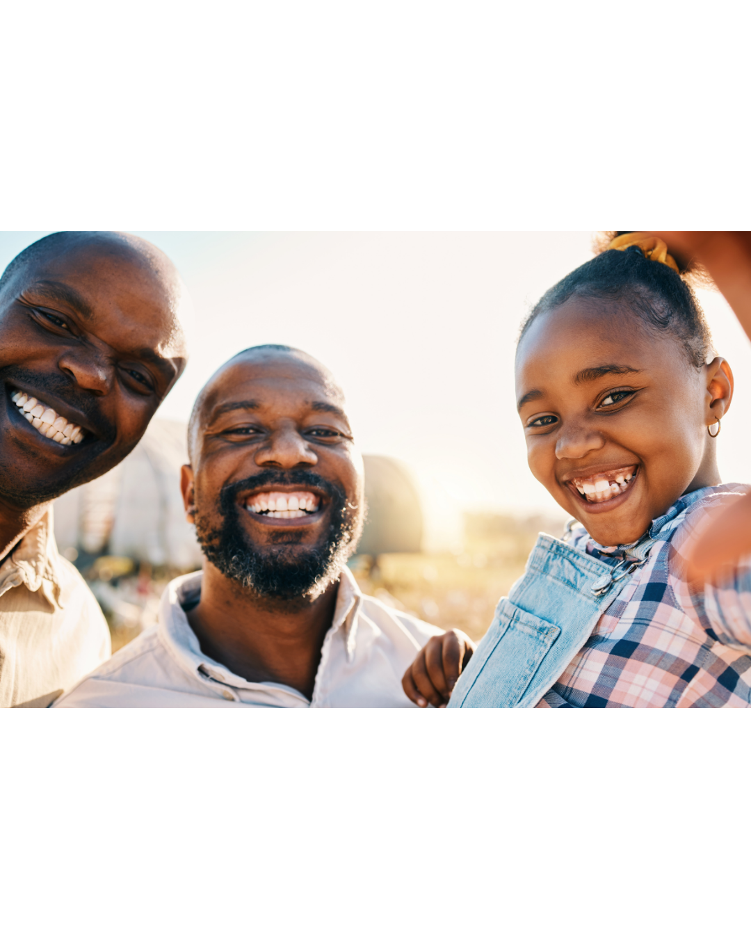 Three adults and a young girl smiling outdoors during sunset.