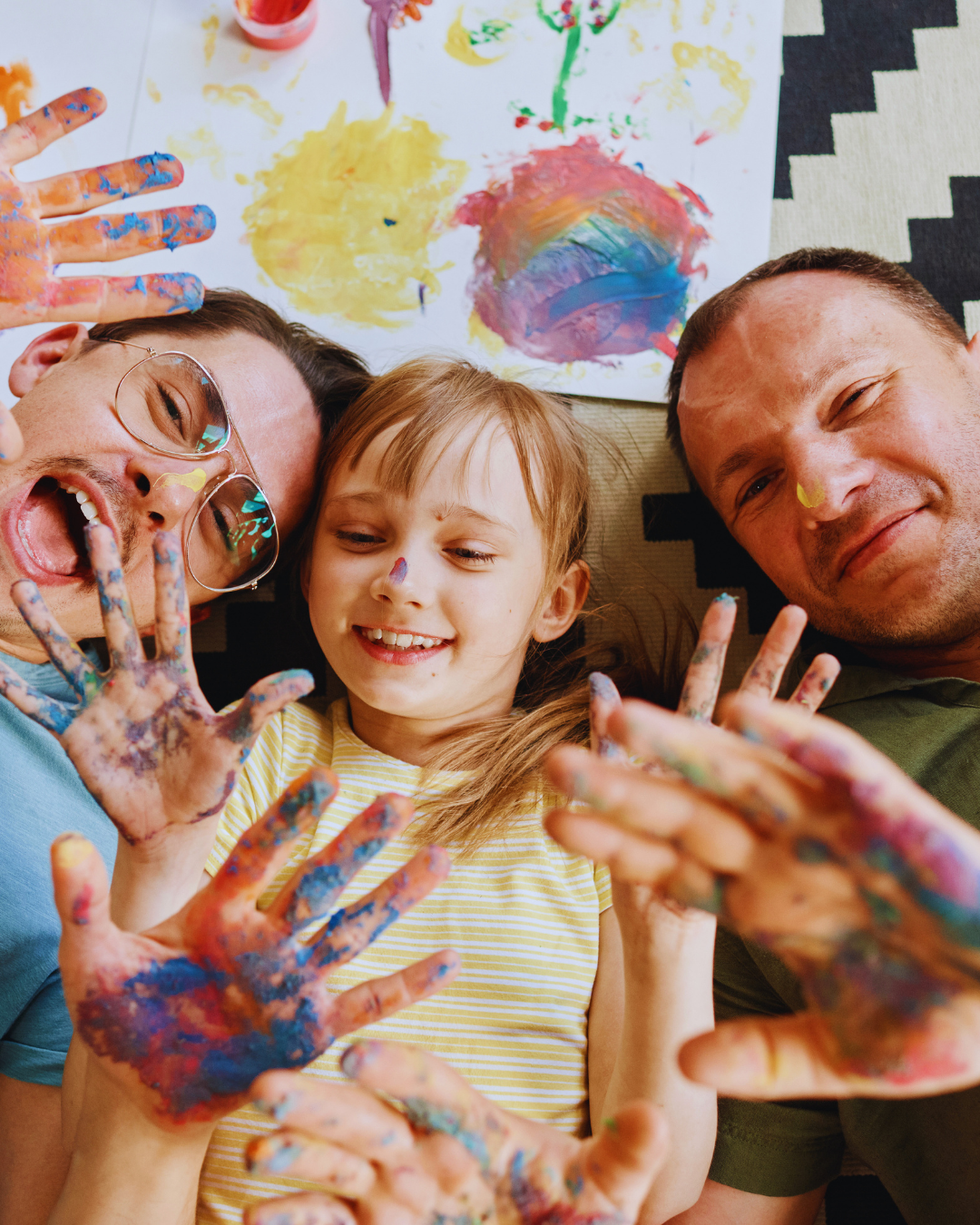 Family lying on the floor with painted hands, smiling and enjoying finger painting.