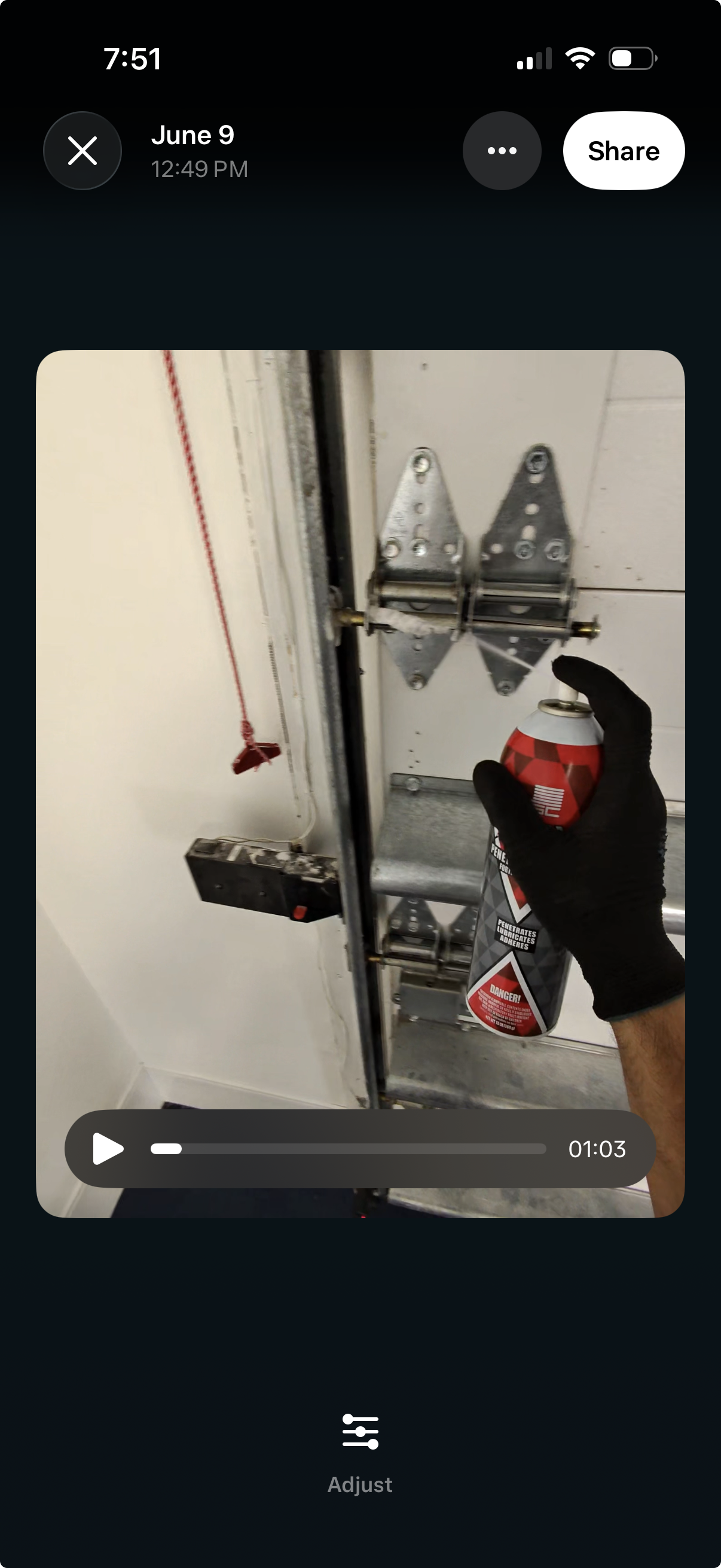 A person holding a can of spray foam adhesive in front of a garage door hinge mechanism, with a red string pull and electrical wiring nearby.