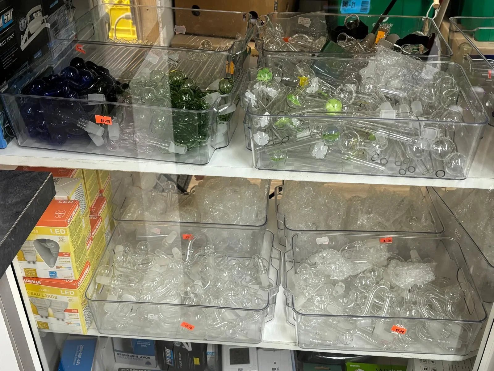 Clear glass and plastic light bulb parts, including bulbs and sockets, organized in transparent bins on store shelves.