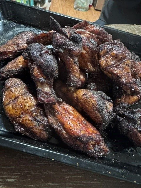 Fried chicken wings seasoned with spices on a black tray.