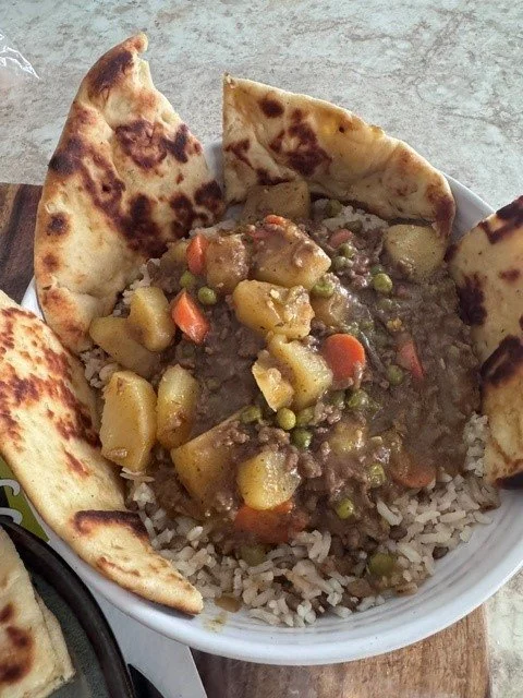 A bowl of rice topped with beef and vegetable stew, surrounded by naan bread.