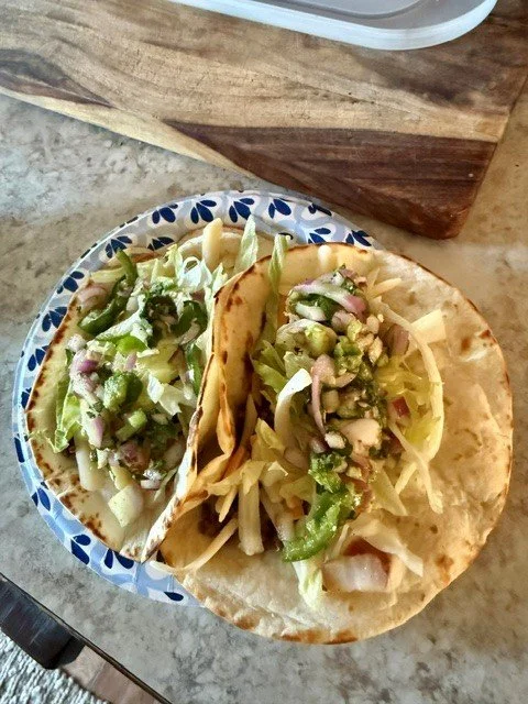 Two tacos on a decorative plate filled with chopped lettuce, green bell peppers, onions, and cheese in a soft tortilla shell.