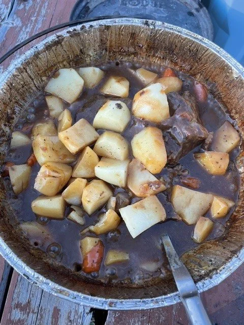 A pot containing a stew with large chunks of potatoes, carrots, and cooked beef in a brown gravy.