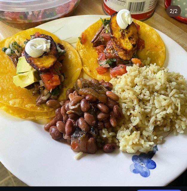 Corn tortillas topped with grilled pineapple slices, diced tomatoes, avocado, and sour cream, served with black beans and rice.