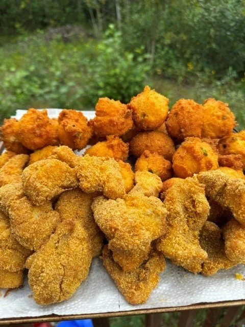 A tray of fried chicken pieces with a green outdoor background.