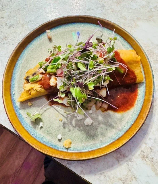 A plate with a Mexican-style breakfast dish, including an omelette topped with salsa and microgreens.
