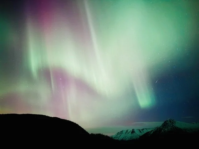 Northern lights in the night sky over mountainous landscape.