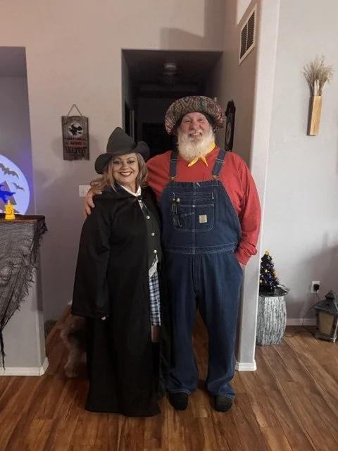 Two people dressed in costumes standing inside a house, smiling and posing for a photo.