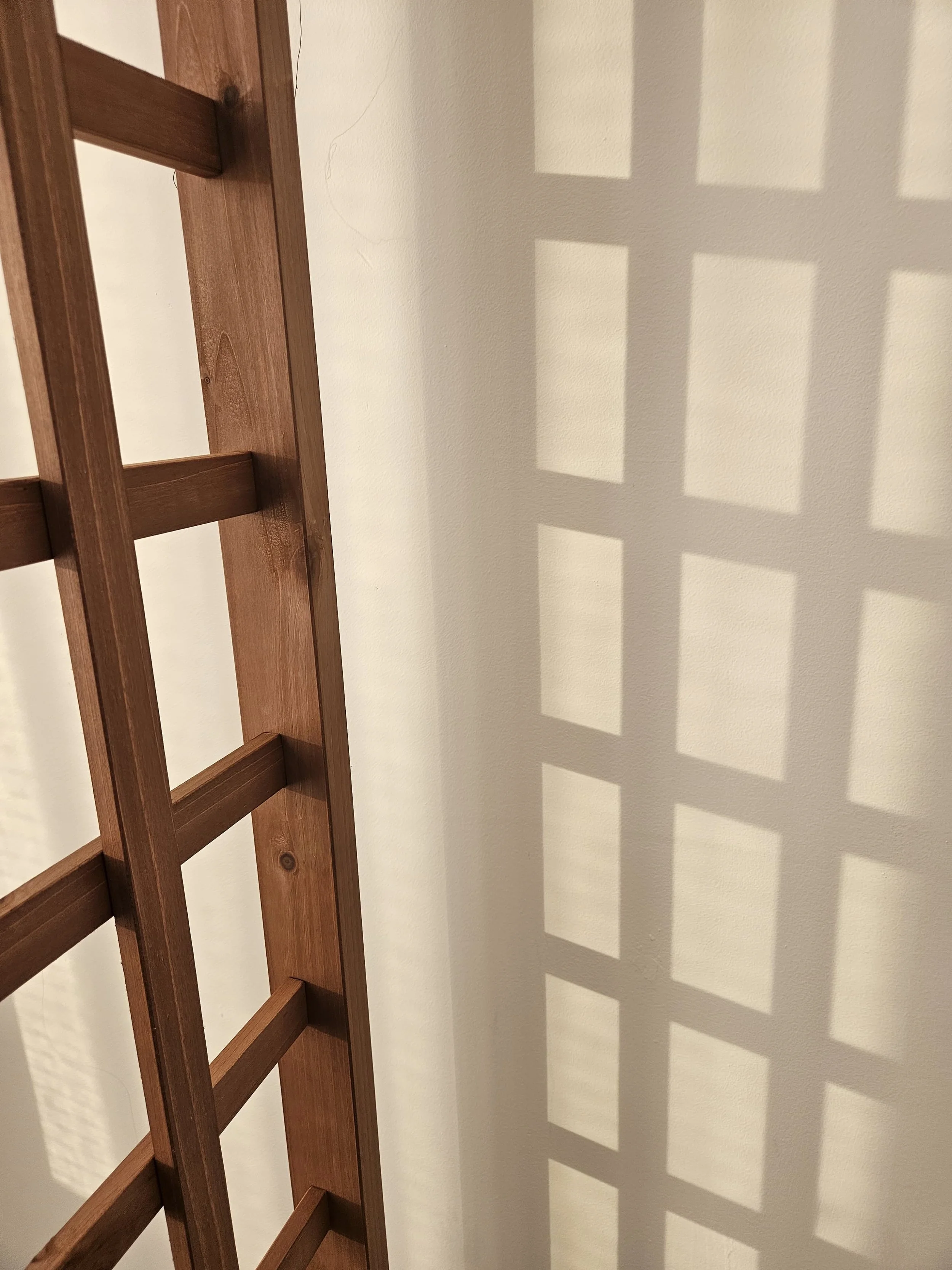 A wooden bed frame leaning against a white wall, casting a tiled shadow pattern in a room.