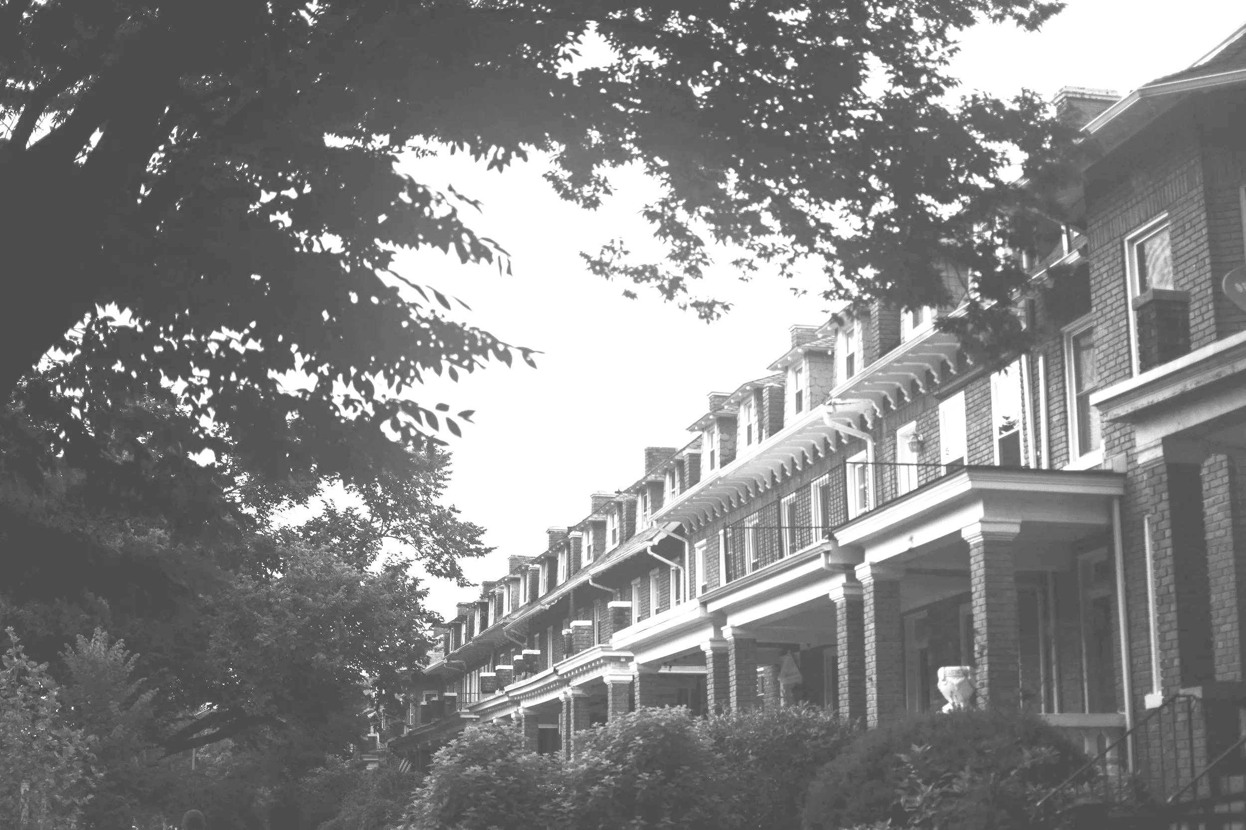 Black and white photo of a multi-story residential building with brick exterior, balconies, and large windows, surrounded by trees.