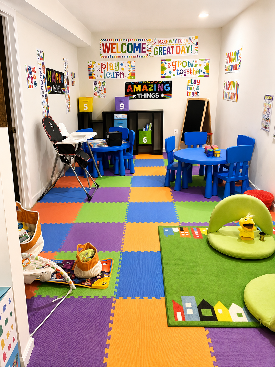 Colorful children's playroom with foam tile flooring, small tables and chairs, toys, and wall posters with positive messages.
