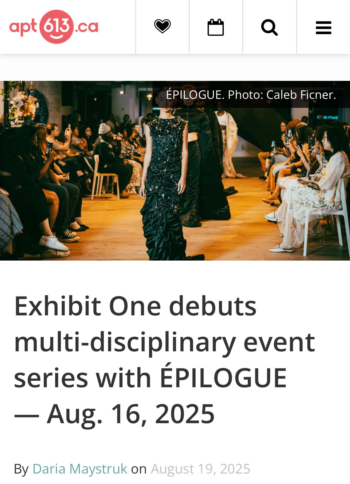 Photograph of a fashion runway show in a gallery-style space, with models walking down the runway and audience members seated on either side, many capturing the moment on their phones.