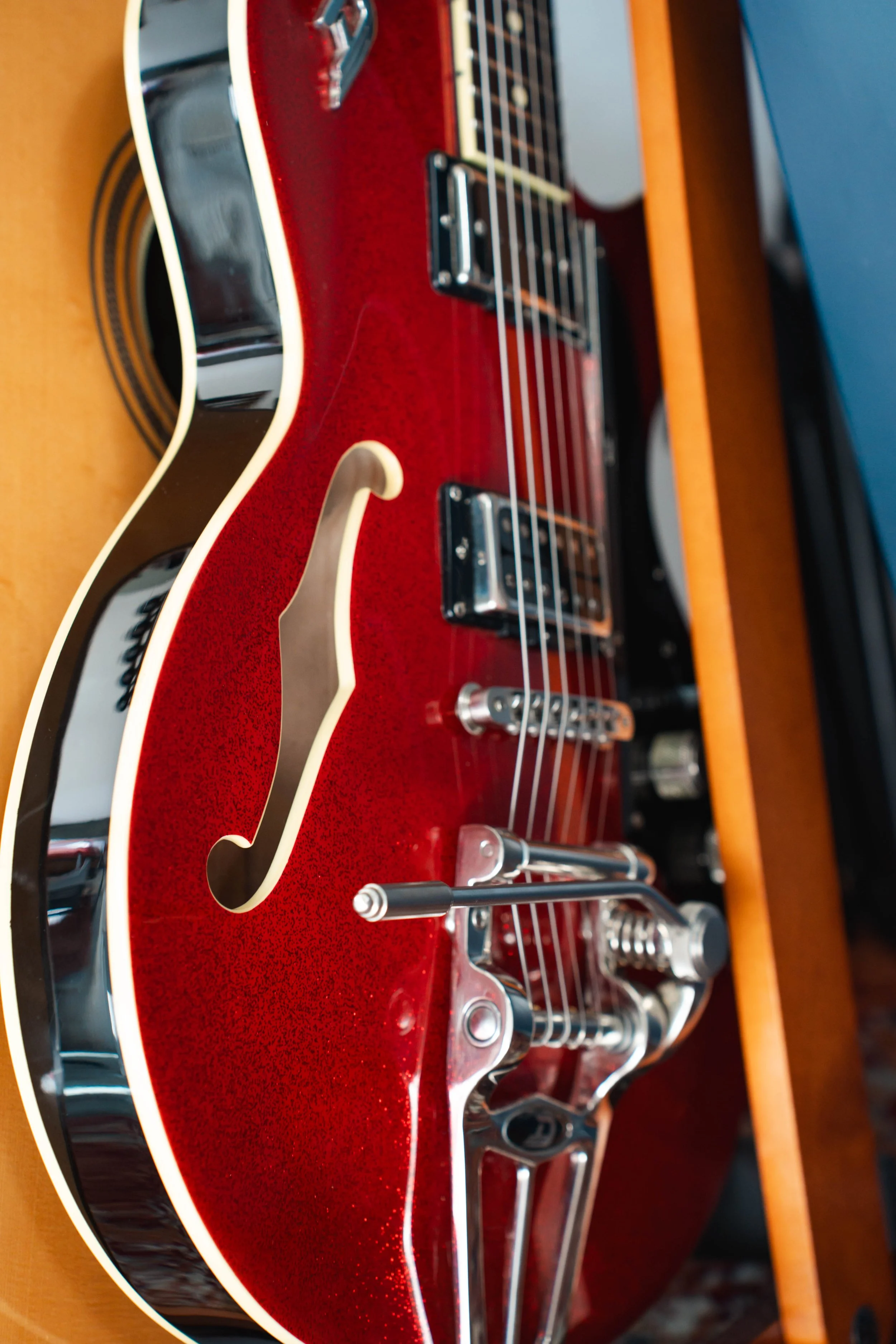 Close-up of a red electric guitar with chrome hardware and pickups, resting on a wooden surface.