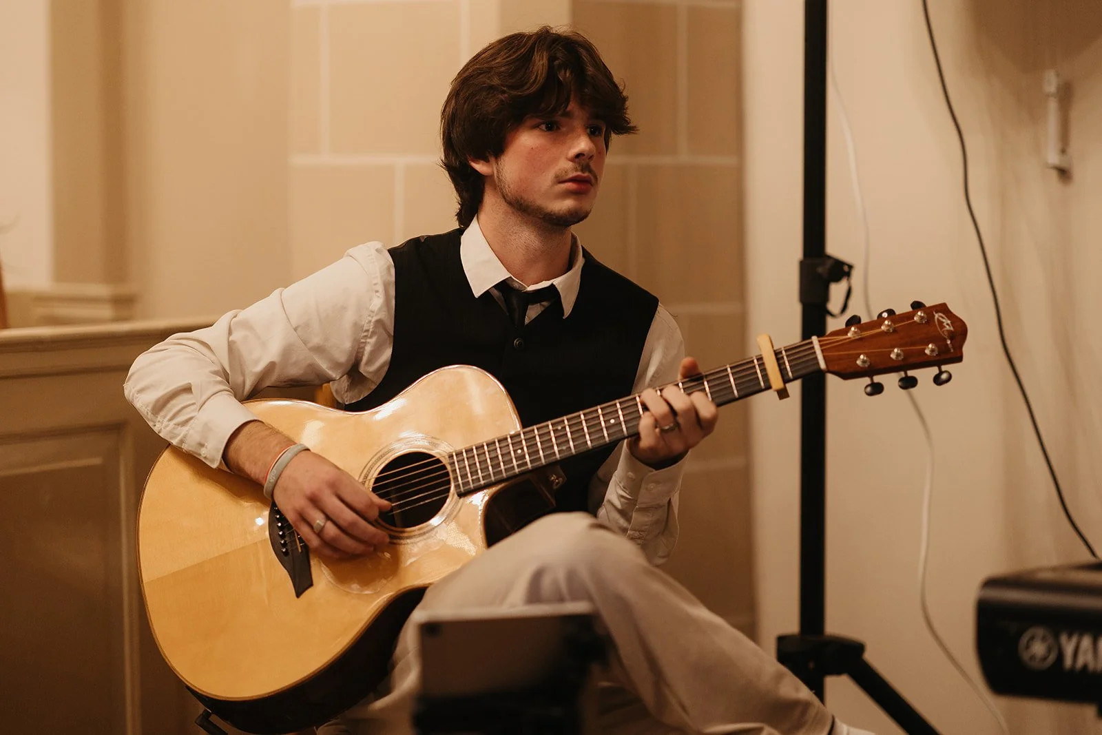 Young man with brown hair playing an acoustic guitar in an indoor setting.