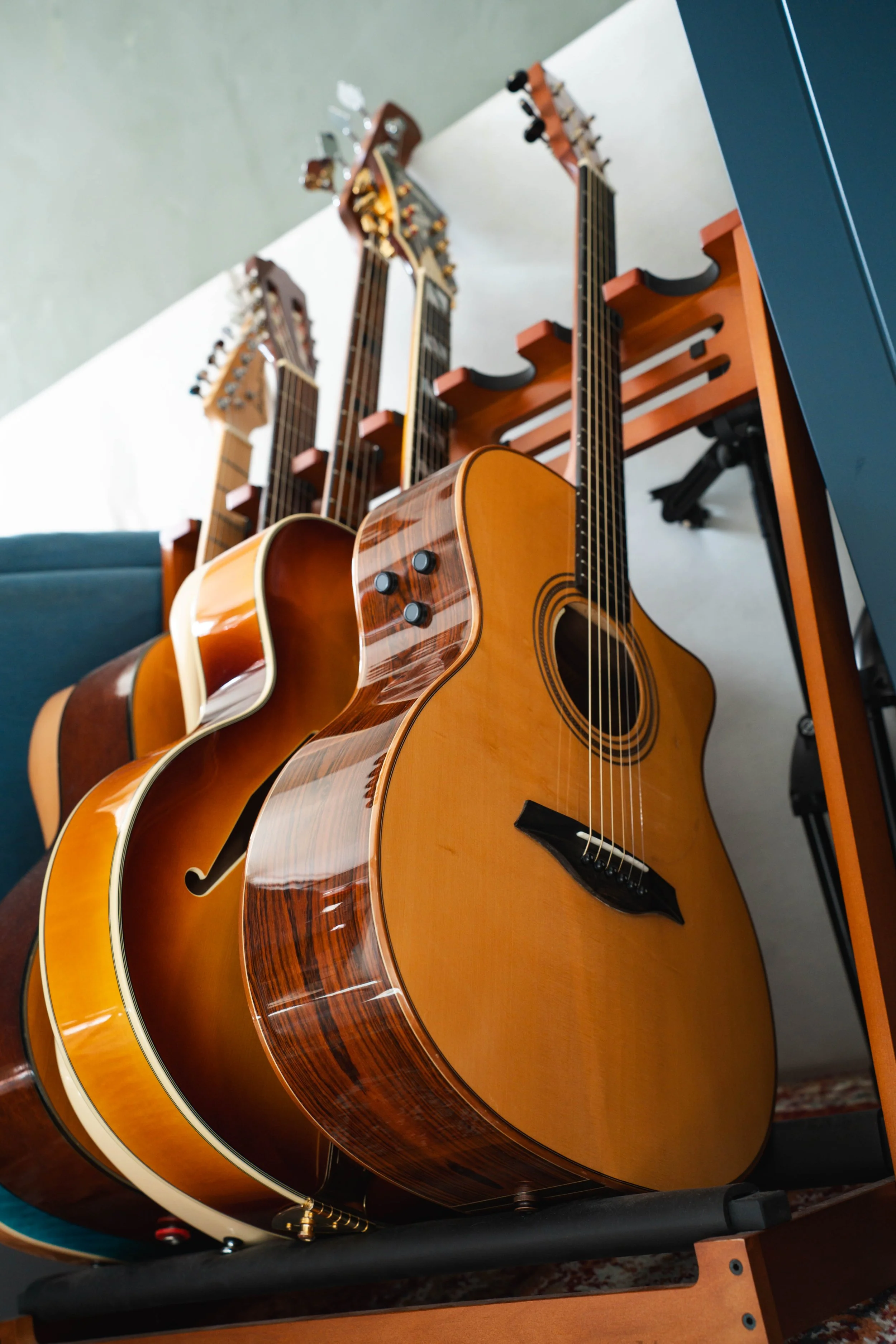 Multiple acoustic guitars arranged on a stand in a room with a white and gray wall background.