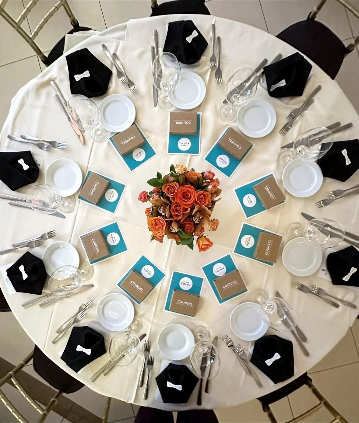 A decorated banquet table set with glassware, plates, and menus, arranged in front of a floral centerpiece with an ornate tree adorned with lights and red ornaments in the background.