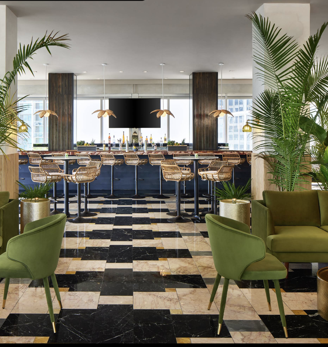Modern bar area with high wooden chairs, green armchairs, potted plants, and a large flat-screen TV, with a city view through windows.