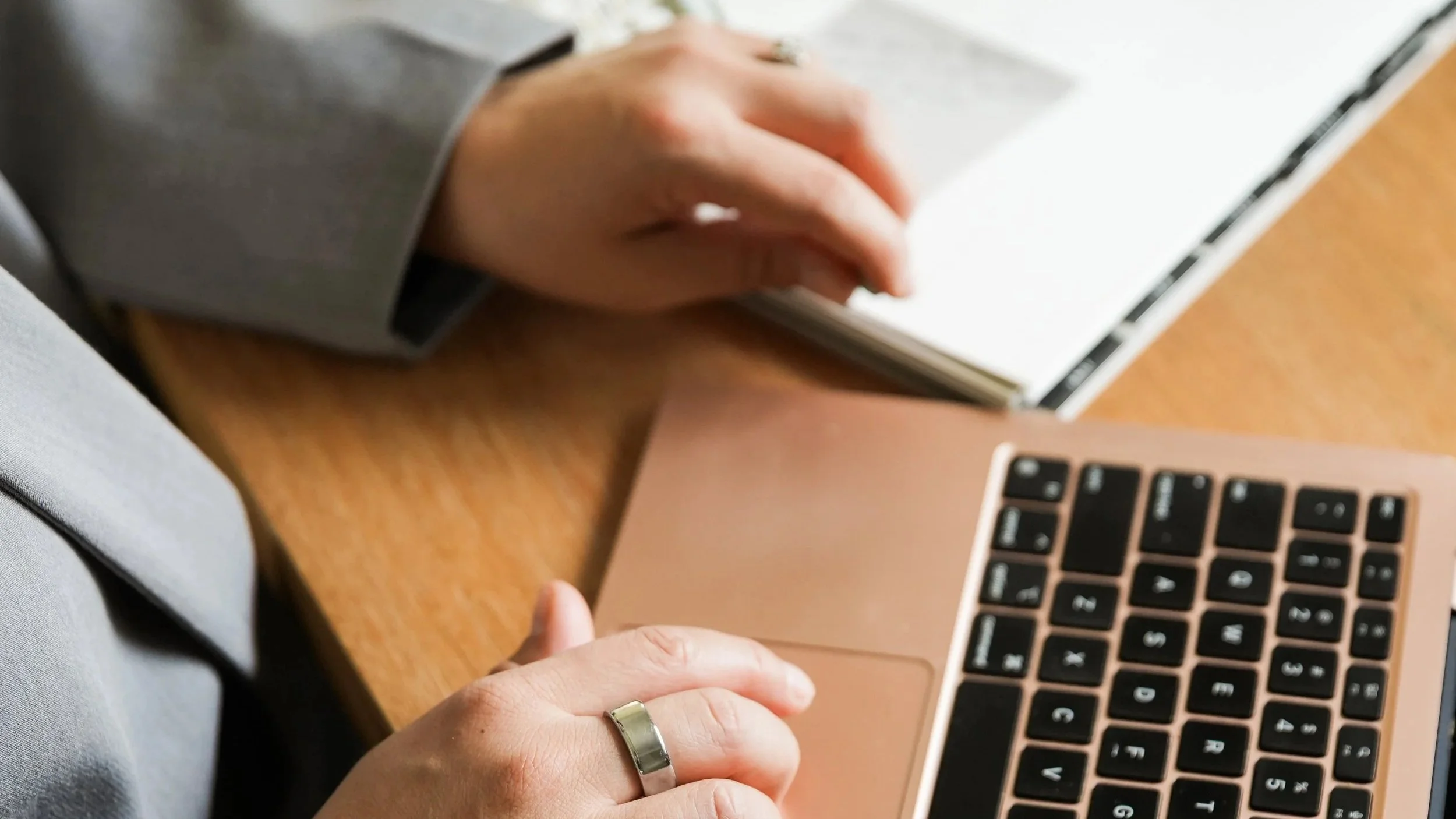 Close-up of hands working with a laptop and notebook at a wooden table.