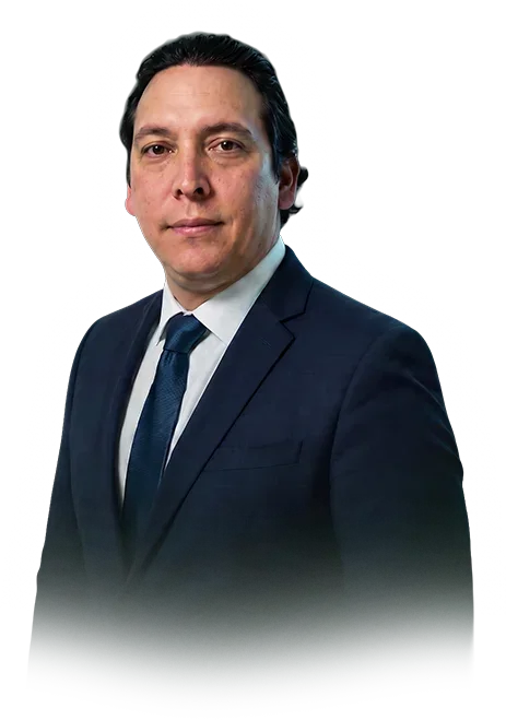 Hombre con traje azul, corbata azul y camisa blanca, posando contra fondo negro.