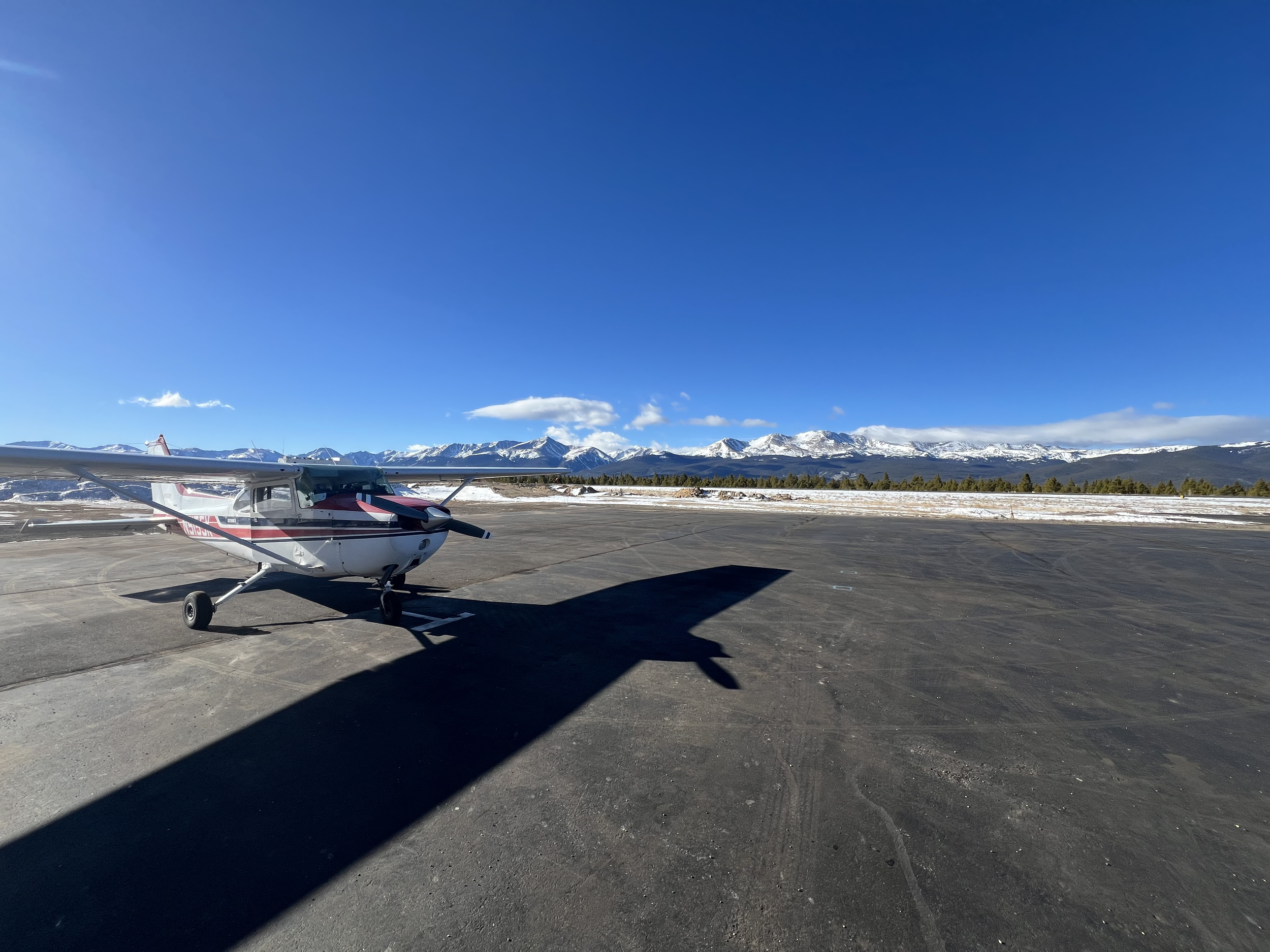 Small aircraft parked on tarmac with snow-capped mountains in the background under a clear blue sky.